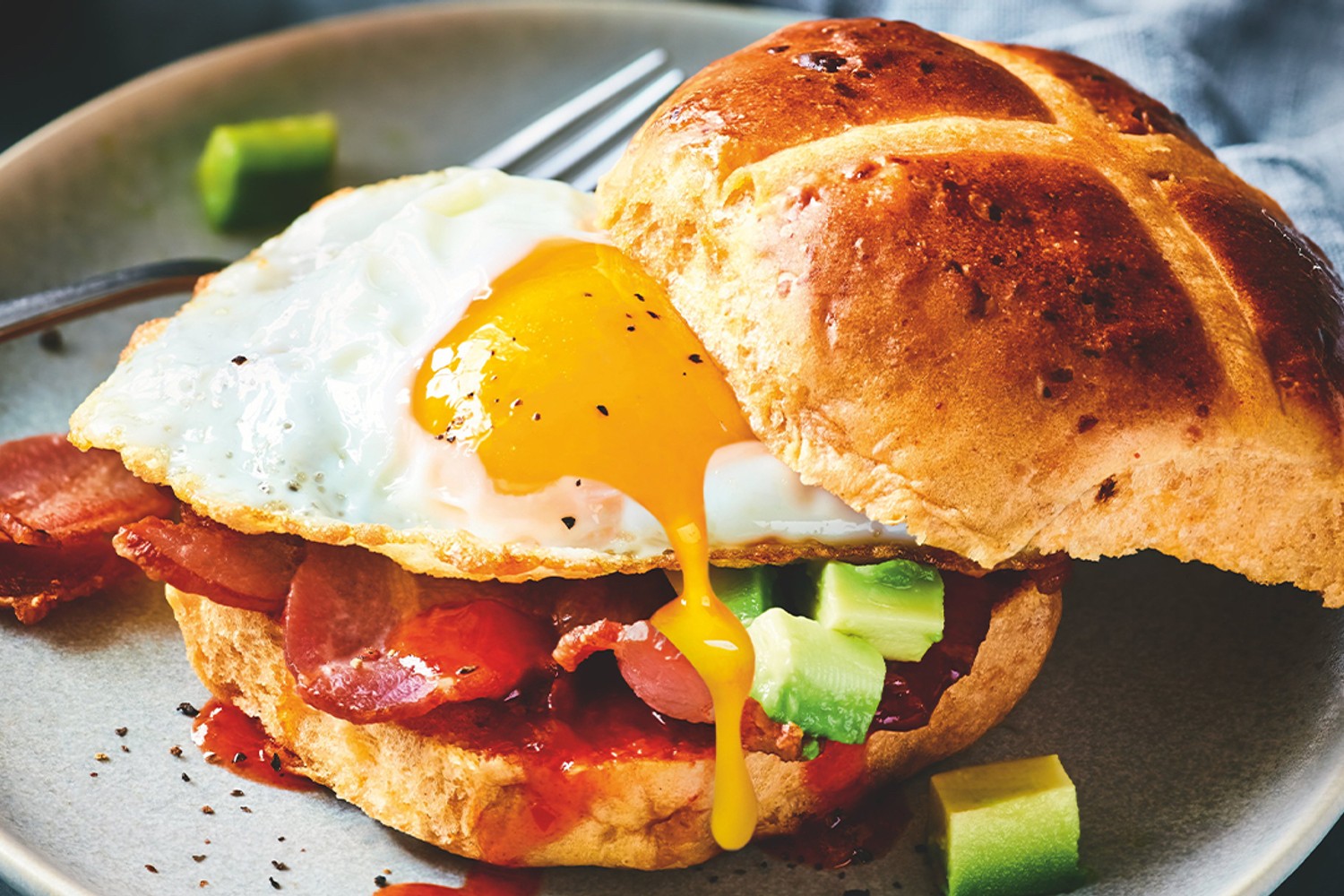 Crispy bacon, avocado, fried egg hot cross bun
