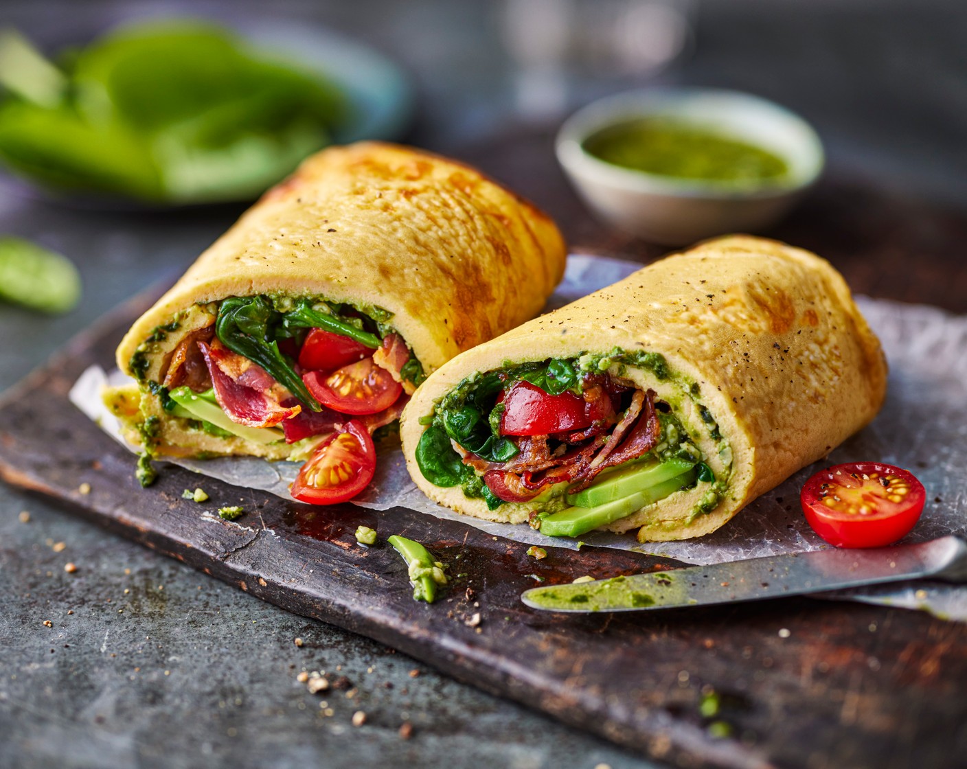 step 4 Spread the pesto (2 tbsp) onto the wrap and then add the spinach, tomatoes, bacon and avocado. Roll into a wrap, cut in half and serve.