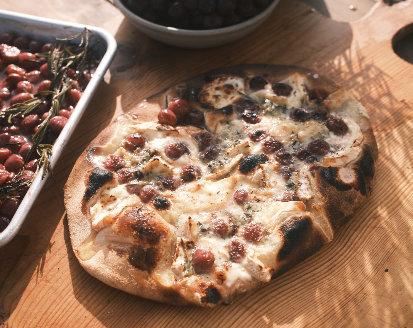 step 5 Carefully transfer the pizza bases onto the preheated oven trays, and working quickly, top each piece of dough with the grapes and rosemary. Crumble over the blue cheese (80 g) and brie (150 g). Pop into the oven for 10-12 minutes, or until the dough has risen and is golden and crisp. Remove the flatbreads from the oven and cut into wedges. Serve immediately, drizzled with a bit of honey (1 tbsp).