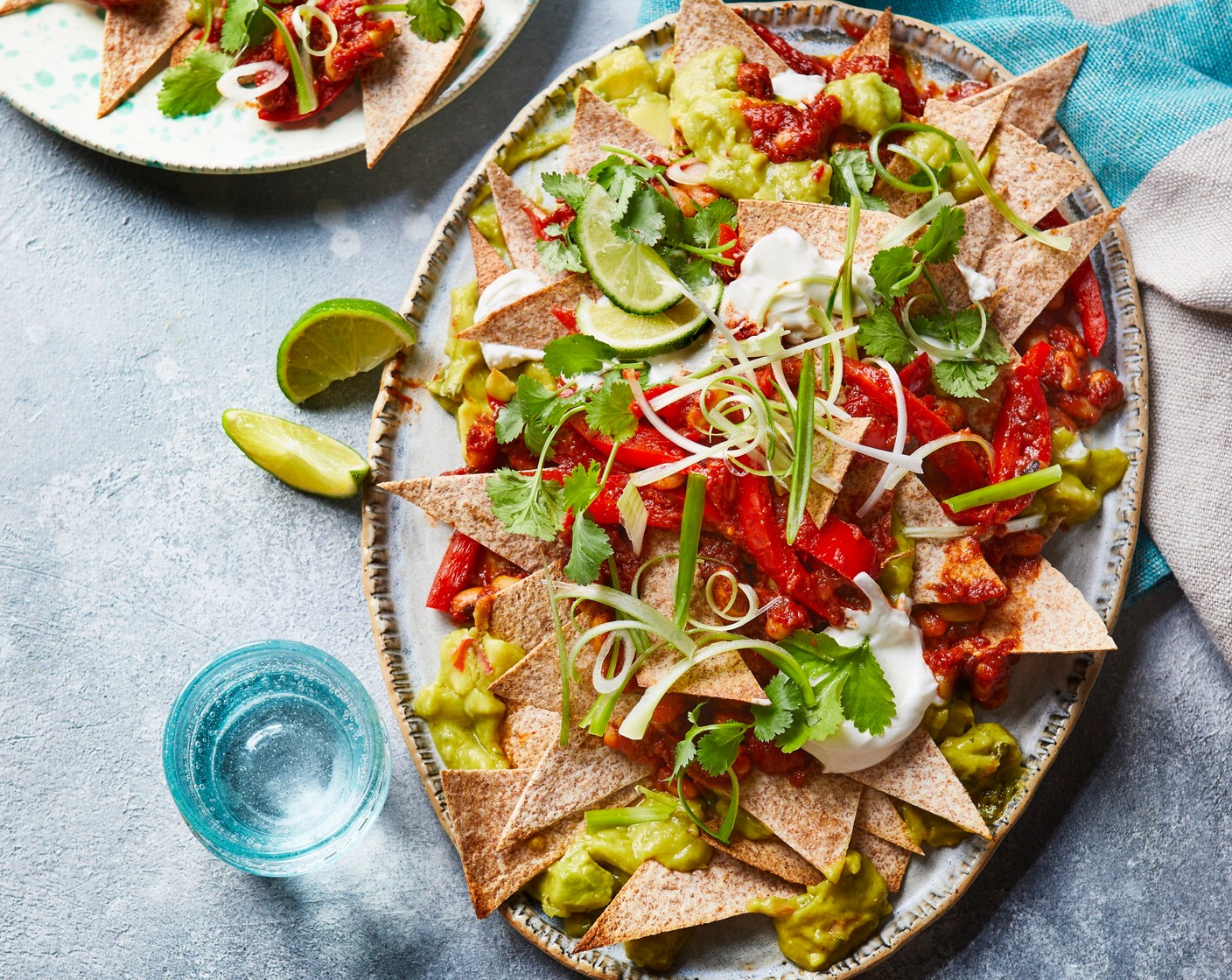step 4 Assemble the nachos by arranging the baked tortilla chips in a bowl and layering with the spicy beans, yogurt (130 g) and guacamole (120 g). Finish with a sprinkling of spring onions (2) and coriander (1 handful) and serve with the lime wedges (1).