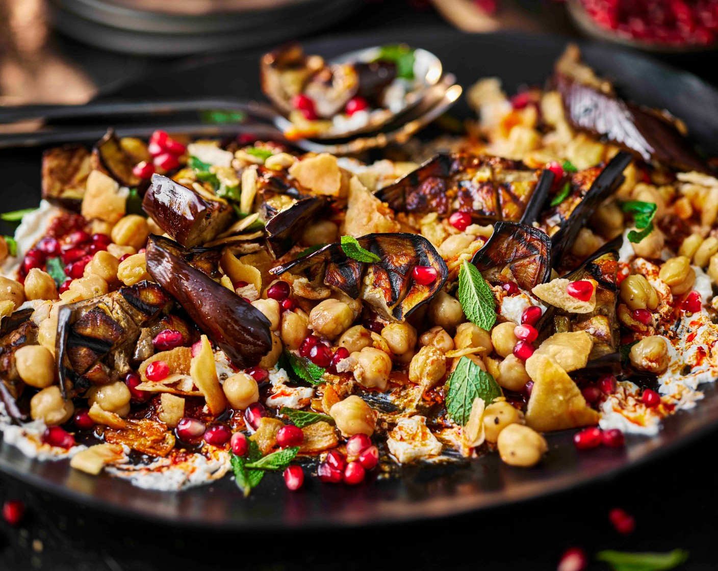 step 6 Cut the grilled aubergine into triangular chunks and add to the plate. Drizzle over the pomegranate molasses dressing, crumble over the pitta chips (70 g) and scatter with the mint leaves (15 g) and pomegranate rubies (100 g).