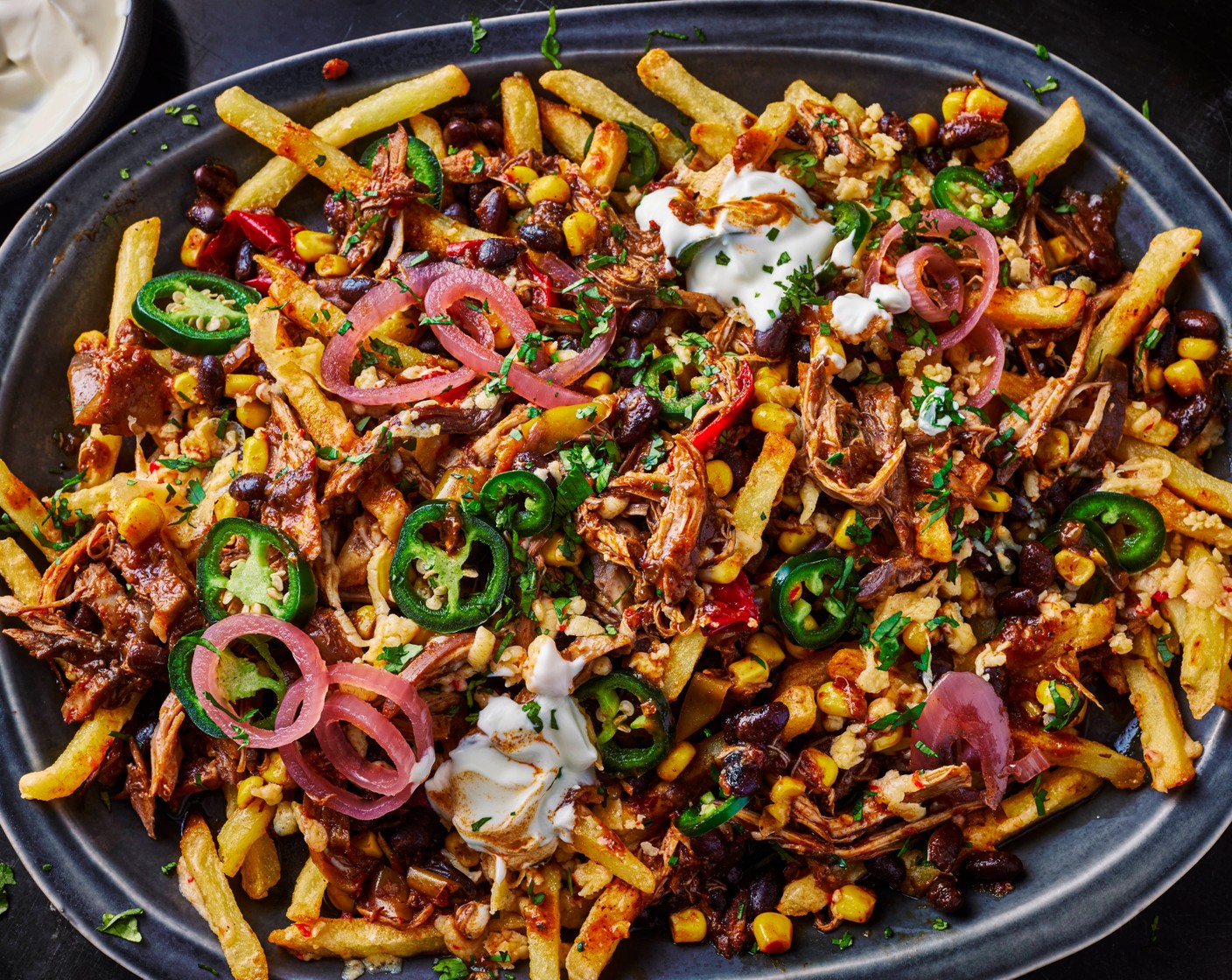 step 6 Serve the fries on a large baking platter and top with half the cheddar (80 g), followed by half the pulled chicken chilli (save the rest for another recipe), the remaining grated cheddar, the sour cream (2 tbsp), jalapeños (1 tbsp), pickled red onions (2 tbsp) and coriander (15 g).