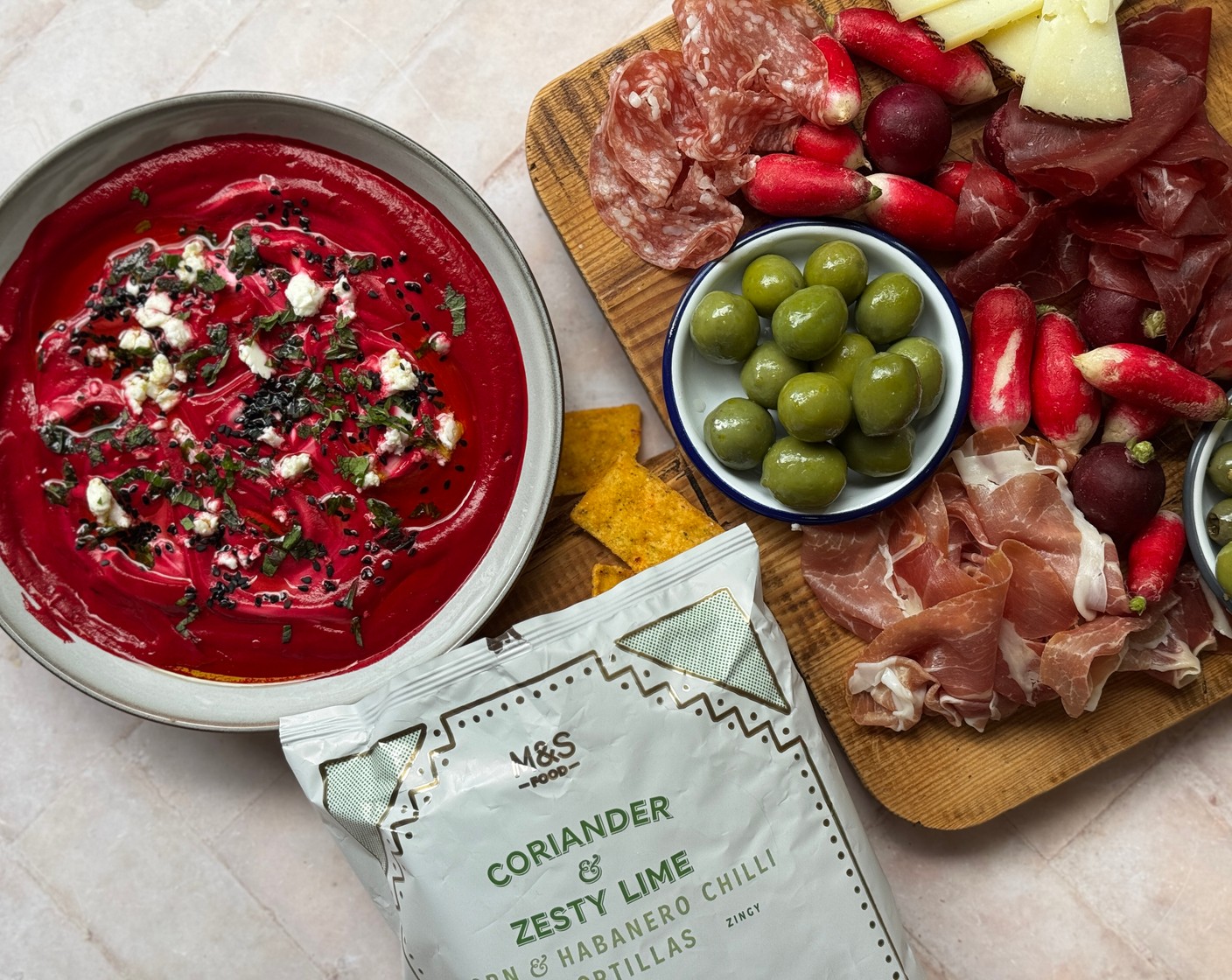step 3 Drizzle over a little more olive oil and garnish with the mint (10 g) and remaining feta crumbled over the top. Arrange the radish (200 g), Manchego (150 g), olives (100 g), prosciutto (70 g), serrano ham and cheese rollitos (10) and tortillas (1 pack) on a grazing board and serve immediately with the dip.