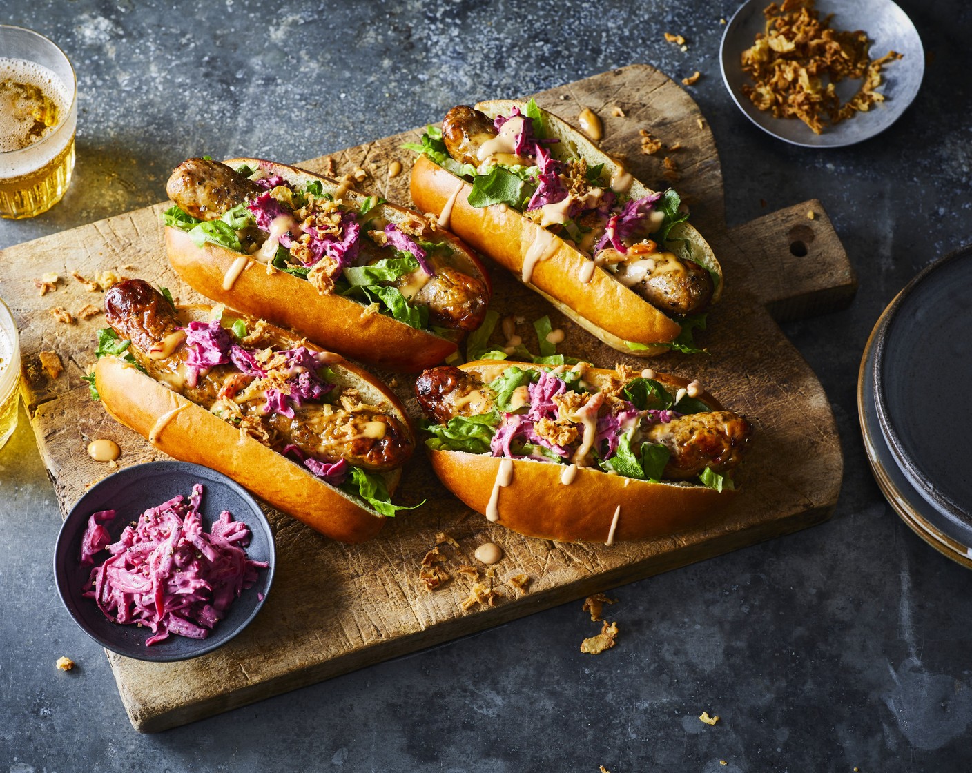 step 3 Cut each brioche roll (4) ¾ of the way through down the centre, then put a lettuce leaves (1) into each, followed by a sausage. Top each roll with a generous amount of the mayo mix and a dollop of the slaw (150 g). Finish each with a sprinkling of crispy onions (50 g).