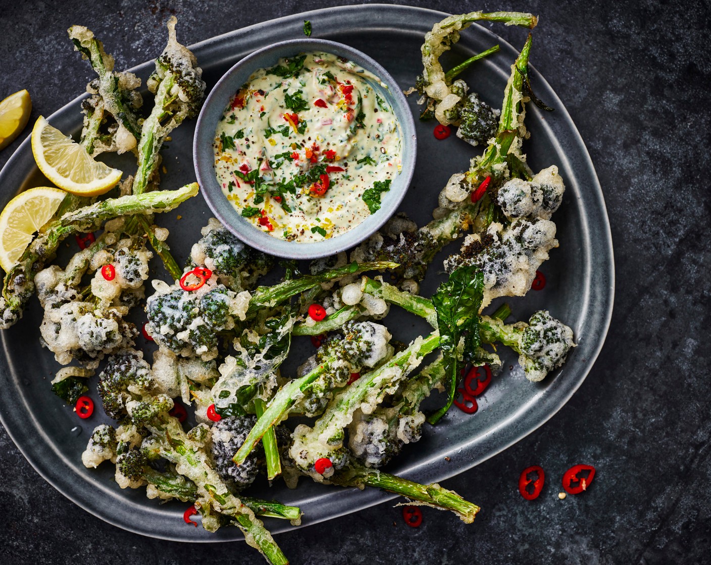 step 5 Add the mayonnaise (100 ml), truffle pesto (3 tbsp), anchovies (2), lemon zest (1), lemon juice (1/2), chillis (1) and parsley (2 tbsp) into a bowl and mix well. Serve this into small bowls and place onto serving plates. Add the broccoli tempura to the plates and sprinkle with a little salt. Add a lemon wedge (as needed) to each plate to serve.