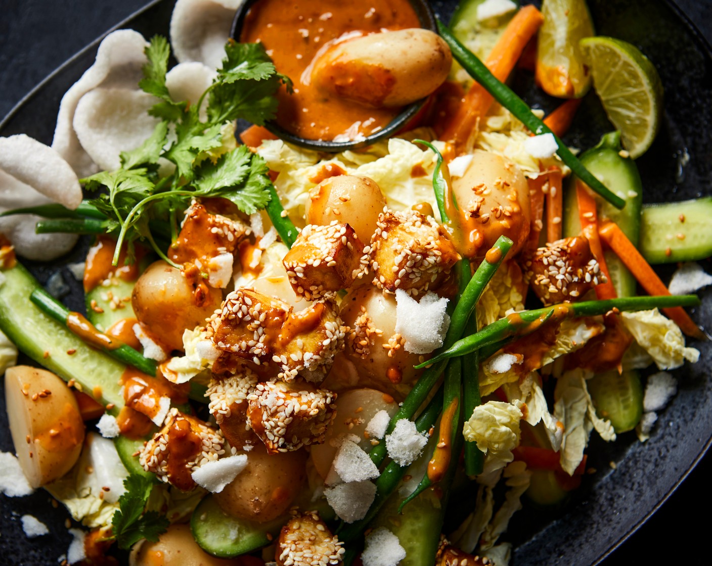 step 5 Arrange the Chinese leaf (1/2), carrots (1) and cucumbers (4) in a large bowl and squeeze over the lime juice (1). Season with salt. Top with the potatoes, green beans and tofu. Drizzle the peanut dressing over the vegetables and tofu. Finish by scattering over some fresh coriander. Crush half of the no prawn crackers (2 handfuls) and sprinkle on top. Serve with the remaining no prawn crackers on the side.