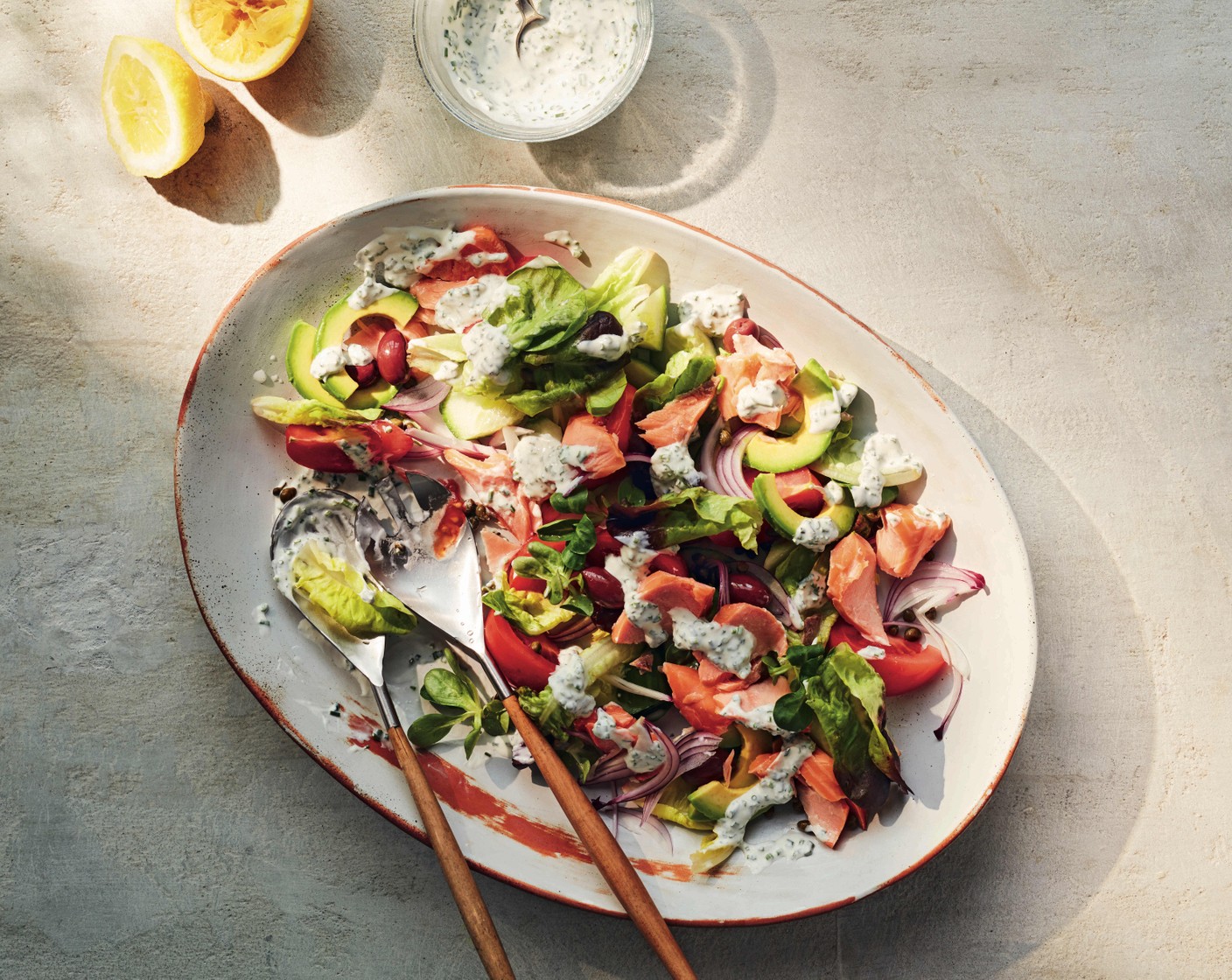 step 2 On a platter, arrange the tomato (3), avocado (2), cucumber (1), onion (1/4), olives (70 g), capers (2 tbsp) and rosa verde (70 g). Flake the hot-smoked salmon (3) into chunky pieces and add this to the plate. Season everything with salt and black pepper and dress with the creamy dressing.