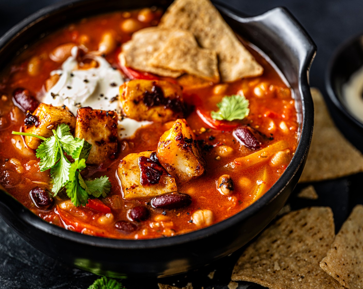 step 6 Serve the soup in bowls topped with the sticky halloumi croutons and a dollop of cooling soured cream (to taste). Scatter over the coriander (5 g) and serve with tortilla chips (80 g) for scooping.
