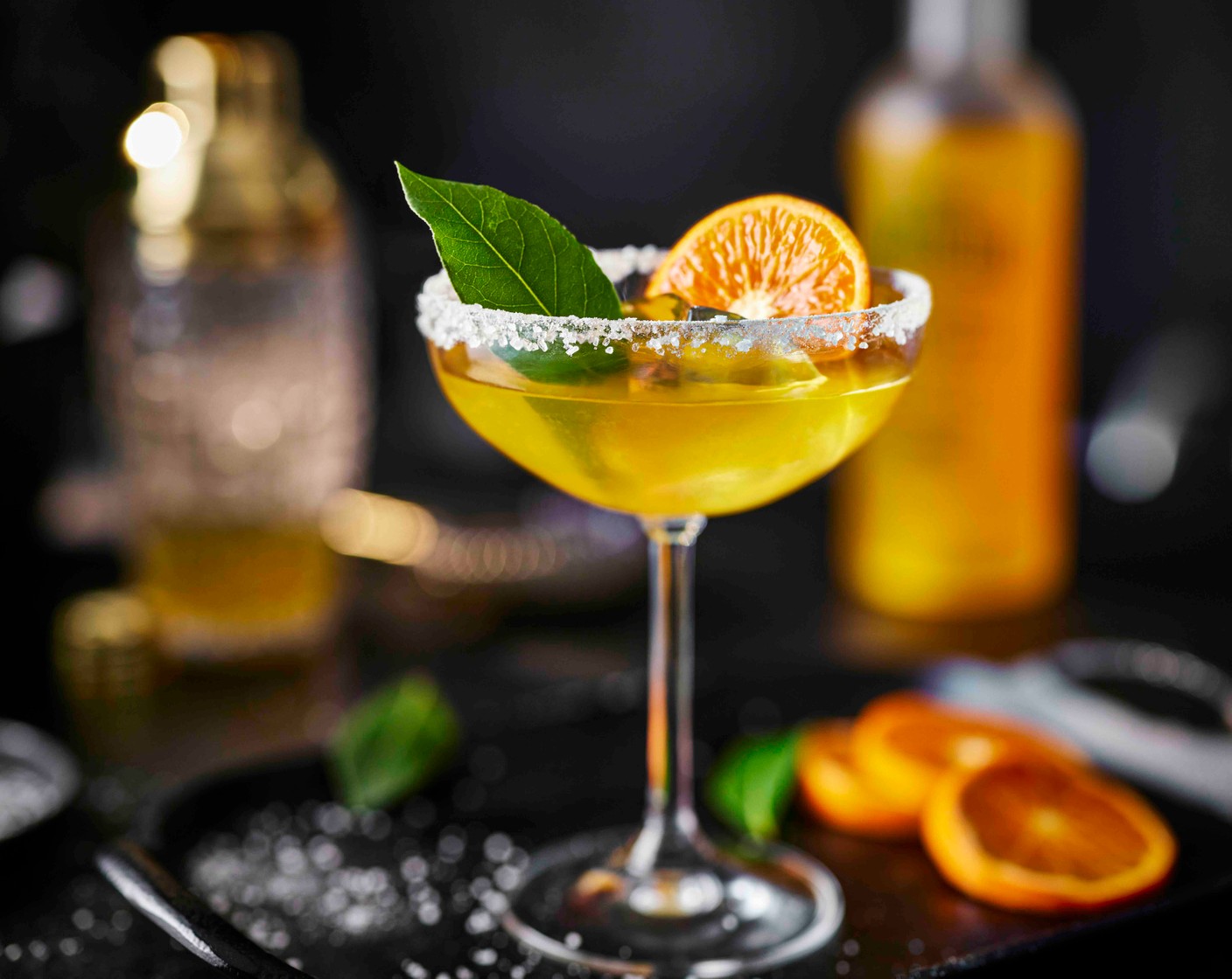 step 4 Fill the prepared coupé glasses with fresh ice. Strain the cocktail evenly between the glasses, then garnish with a bay leaf (2) and a slice of clementine (1).