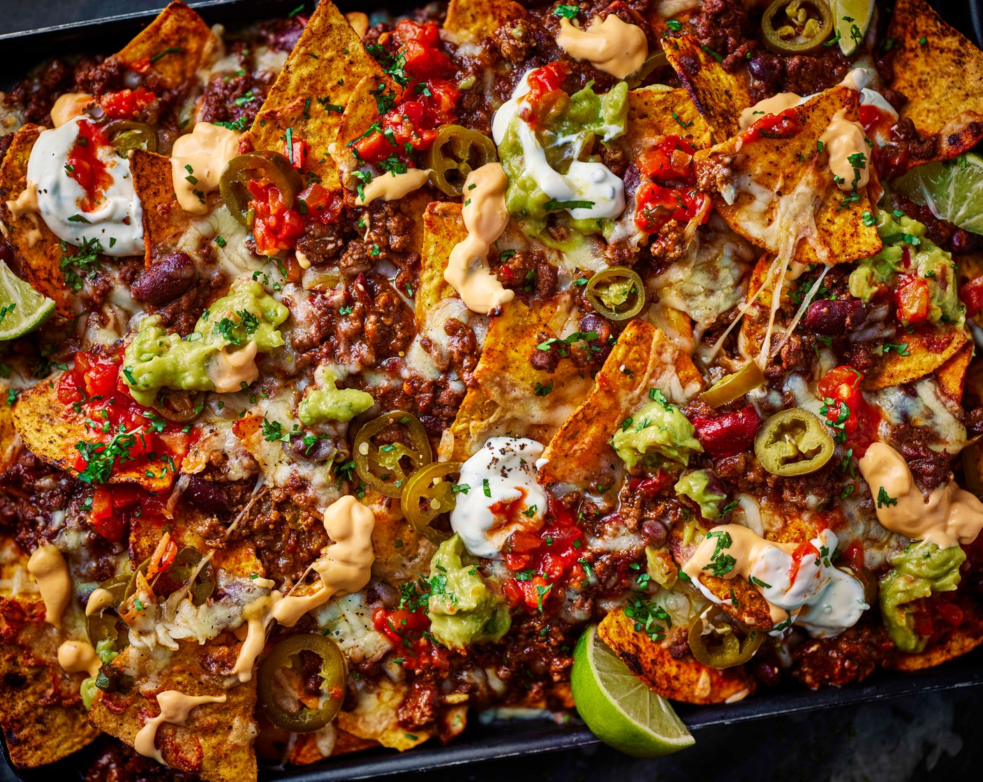 step 5 Remove the nachos from the oven and top with your dips (1 pack) of choice, coriander (15 g) (optional), more jalapeños, lime wedges (1) and season to taste with salt and pepper.