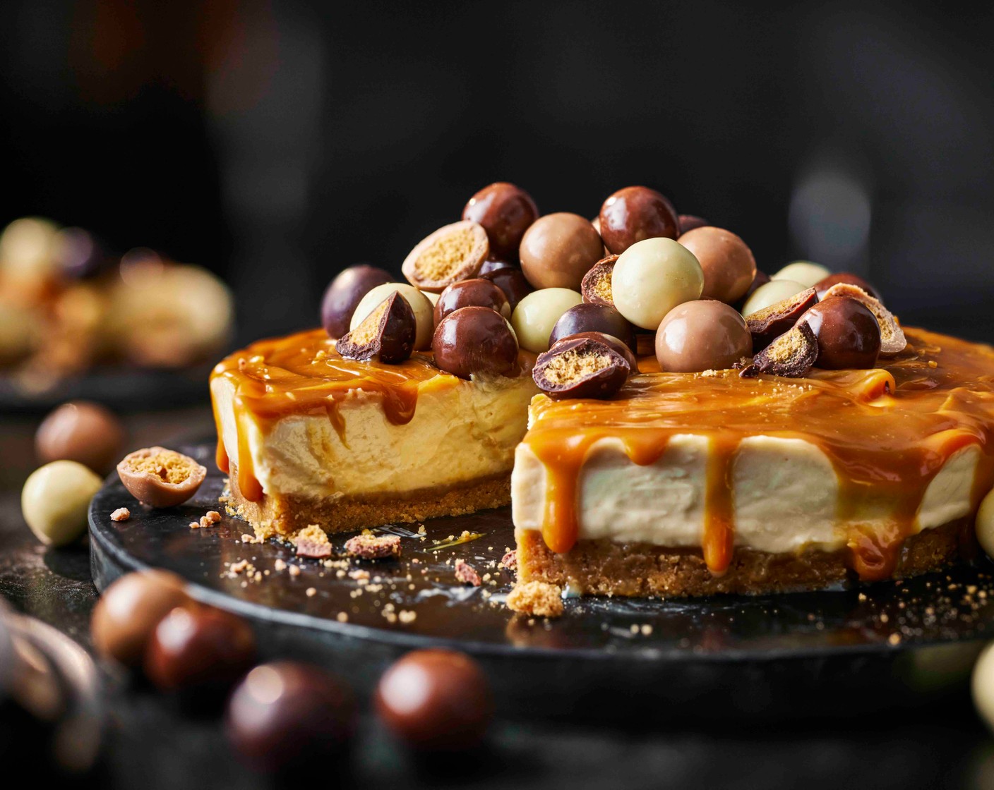 step 4 Warm the remaining salted caramel (120 g) slightly until spreadable, then spoon over the cheesecake. Pile the malt balls (200 g) on top, arranging the different chocolates evenly across the surface. Chill for 15 minutes before slicing and serving.