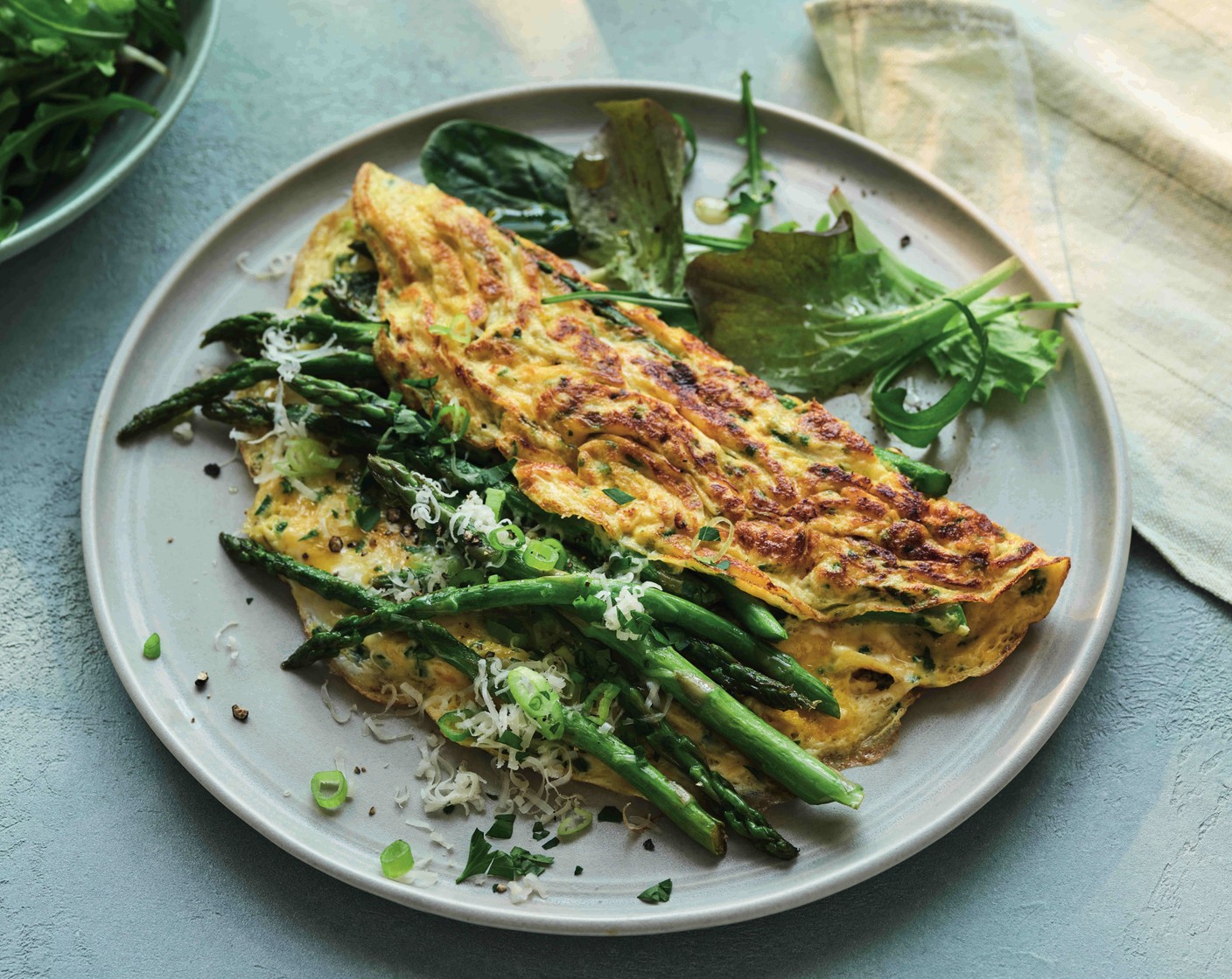 step 4 Scatter the top with the Gruyère (20 g), spring onions (2) and reserved asparagus, then slide the omelette onto a plate, folding it in half as you go. Serve with a leafy salad (to taste).