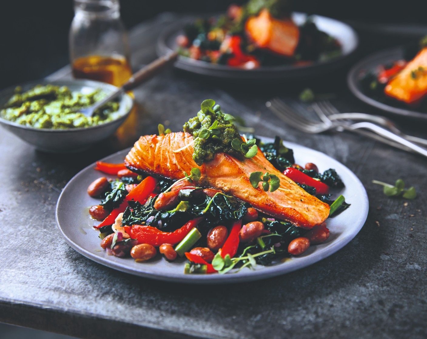 step 7 Spoon the bean stew into the centre of each plate and top with the salmon. Spoon some pesto on top of the fish, garnish with chopped basil and the edible viola flower (1) and dress with a drizzle of olive oil.