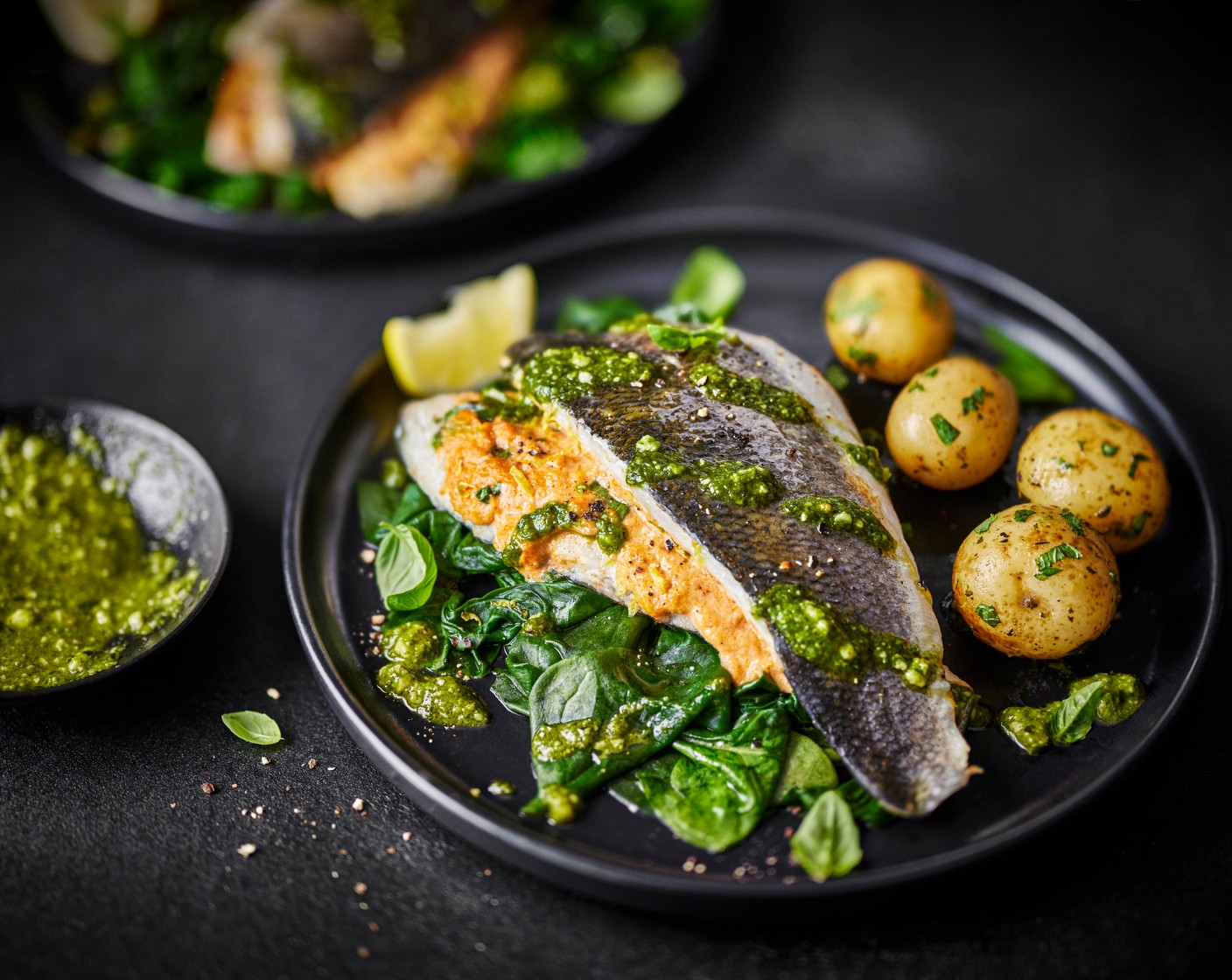 step 7 Once cooked, remove the fish from the tray and carefully remove the cling film. Place the wilted spinach in the middle of your serving plates. Place the seabass on top, skin-side up, and drizzle over the pesto (1/2 tub). Finish with a wedge of lemon (1/2) and the potatoes.