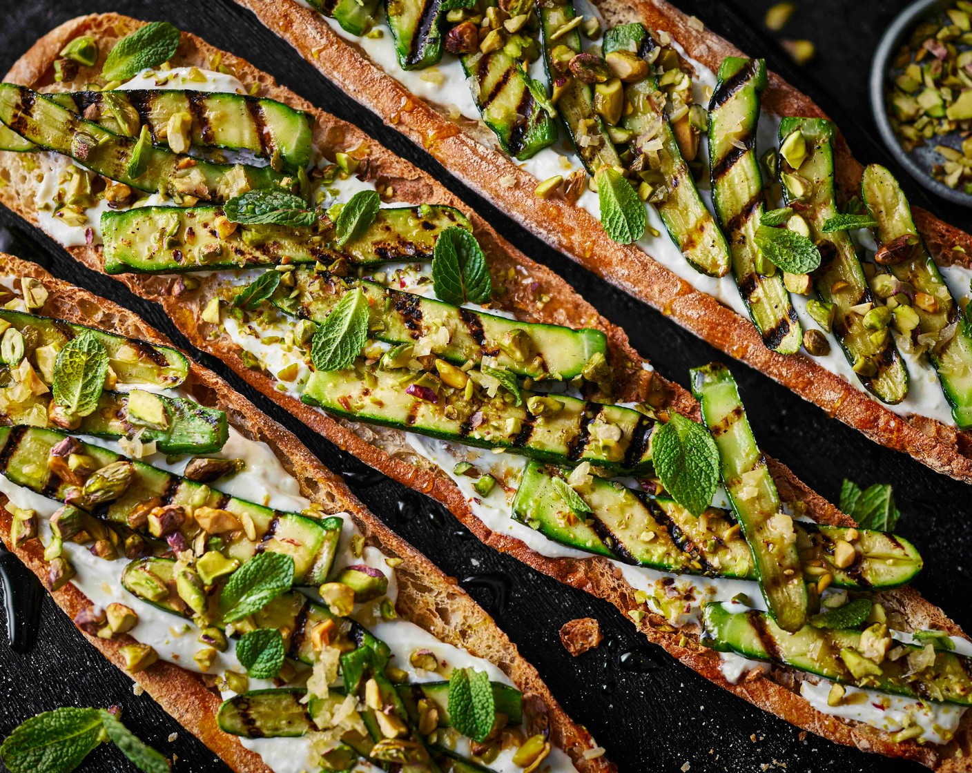 step 3 Top the pan de cristal with a generous layer of whipped feta (200 g), followed by the charred courgettes, preserved lemon (1), torn mint (10 g), a drizzle of chilli oil (as needed), pistachios (4 tbsp) and a light drizzle of honey (as needed).