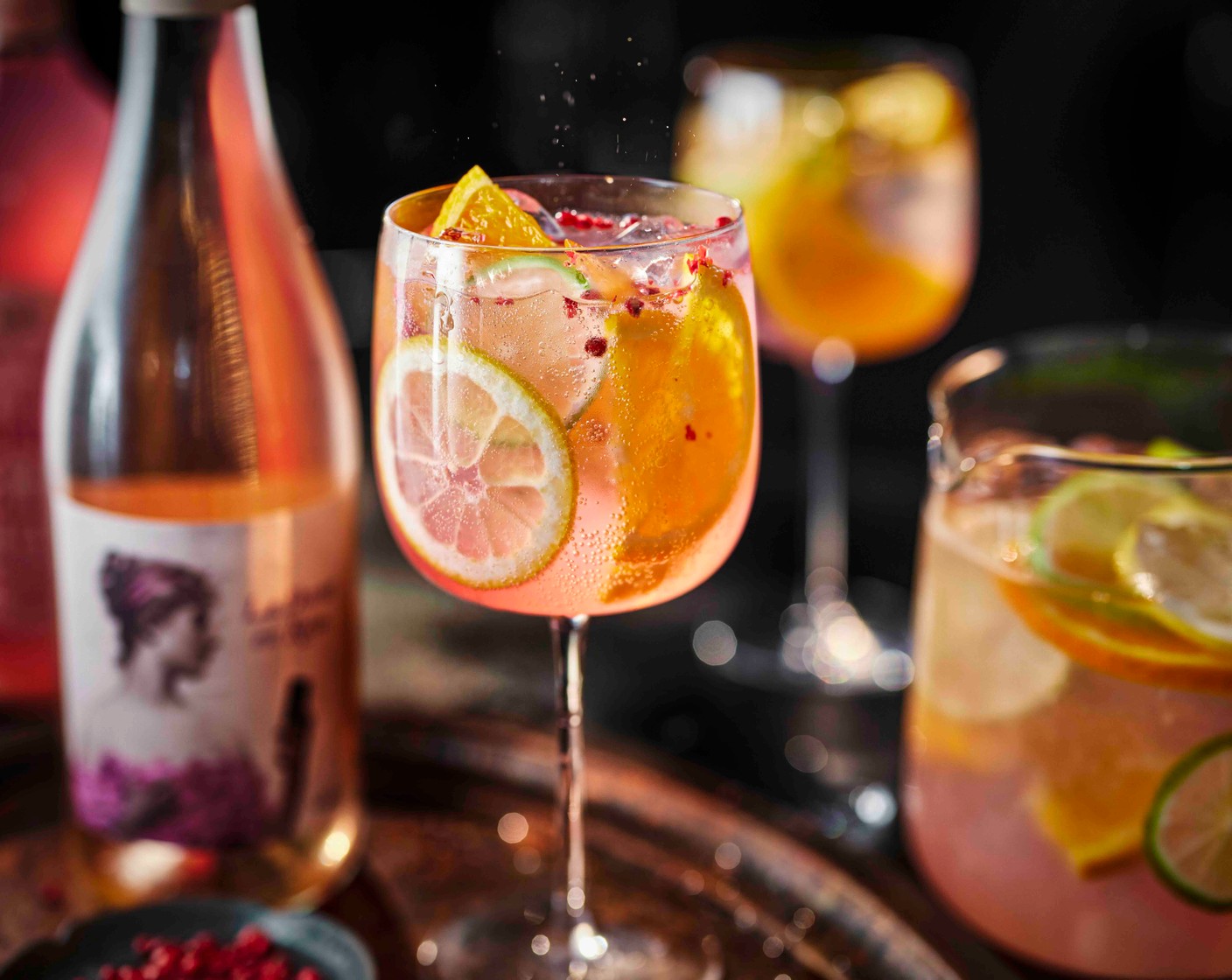 step 1 Add the ice (as needed), sliced limes (2), lemon (1), orange (1), rose (1 bottle) and lemonade (1 bottle) to a jug and stir together. Pour into wine glasses. Top with the pink peppercorns (1 tsp), if you’d like.