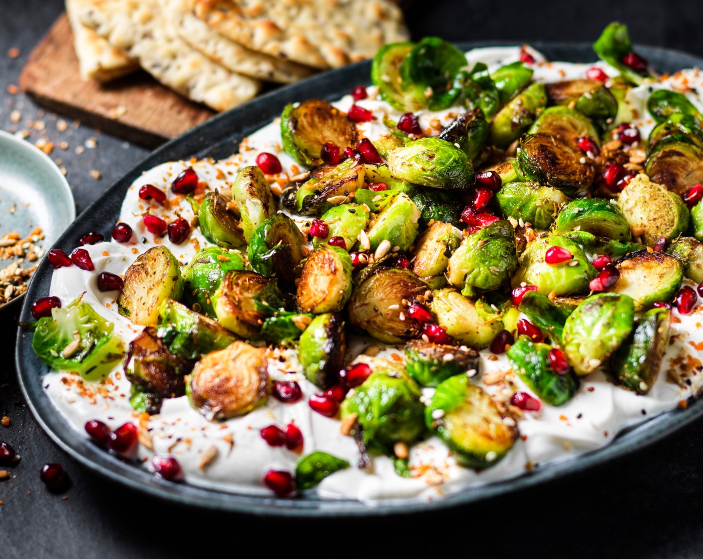 step 4 Remove the sprouts from the oven and place on top of the yogurt, followed by pomegranate (4 tbsp) and dukkah (as needed). Finish with a drizzle of lemon-infused olive oil (as needed) and serve with warm flatbreads (4).