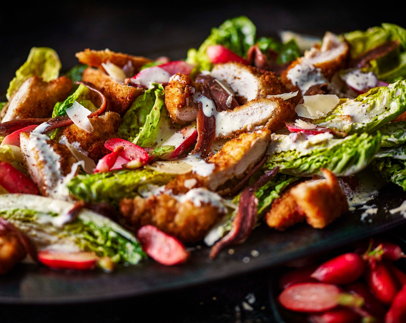 step 5 Slice the chicken tenders and arrange on top of the lettuce. Spoon over the radishes, then arrange the anchovies (1 tin) on top. Shave over the parmesan (30 g) with a speed peeler, add a good crack of black pepper, and the remaining lemon juice (1/4).