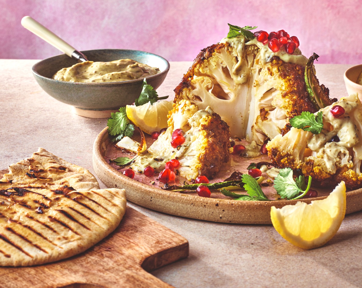 step 5 Carve the cauliflower into quarters. Scatter with coriander (1 handful) and pomegranate seeds (to taste) and serve with the crispy leaves, the roti (2 packs), the raita and the lemon wedges (1) for squeezing.