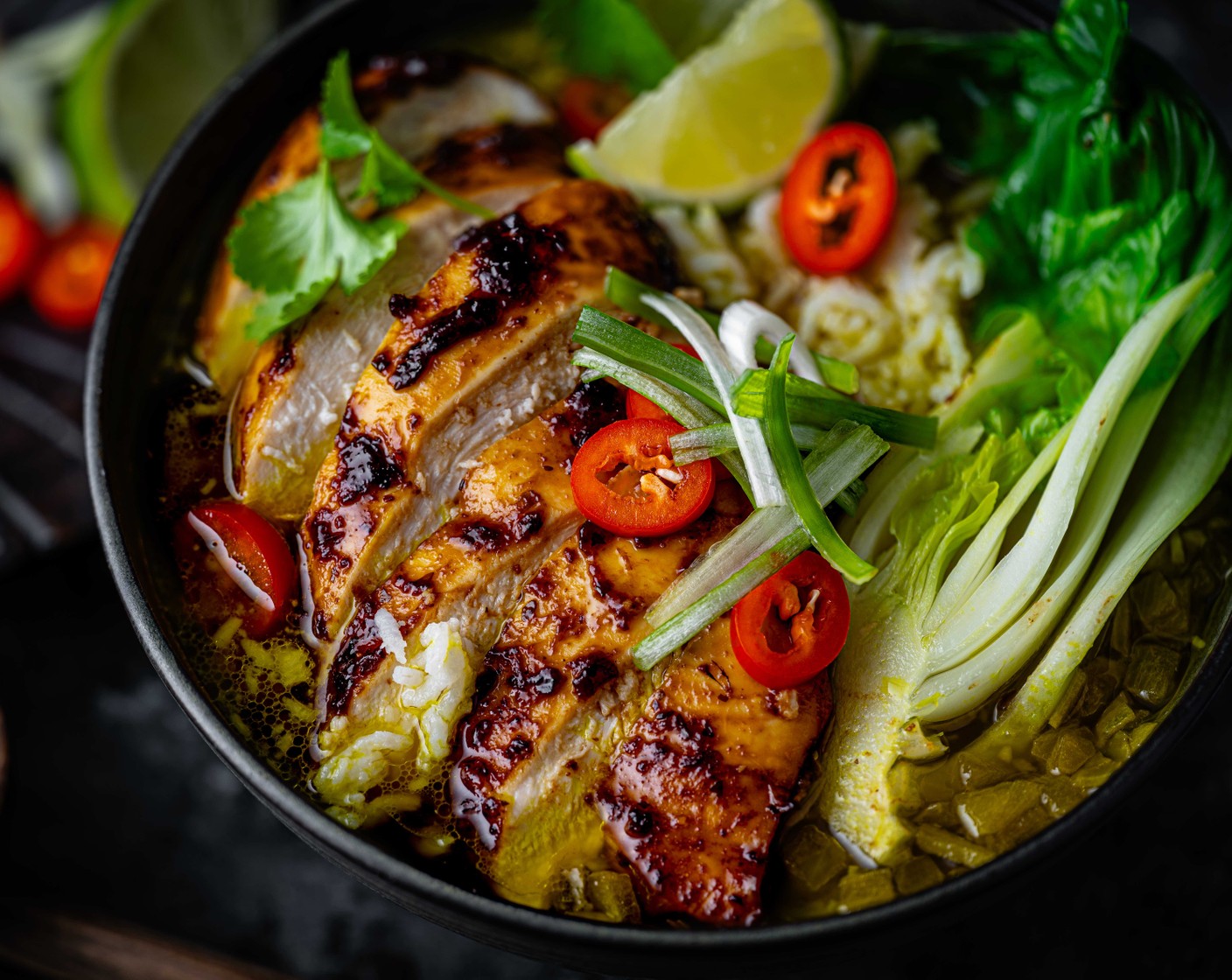 step 4 Take the chicken out of the oven and slice it horizontally. Add the rice to a deep bowl, followed by the pak choi. Top with the broth and add the sliced chicken. Serve with a wedge of lime (1) and a scattering of spring onions (3). Scatter over some chopped chilli (1), if you like.